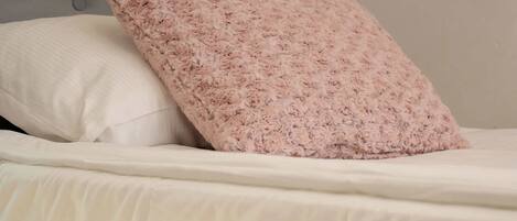 A bed with a tufted headboard, a white pillow, and a fluffy pink pillow.
