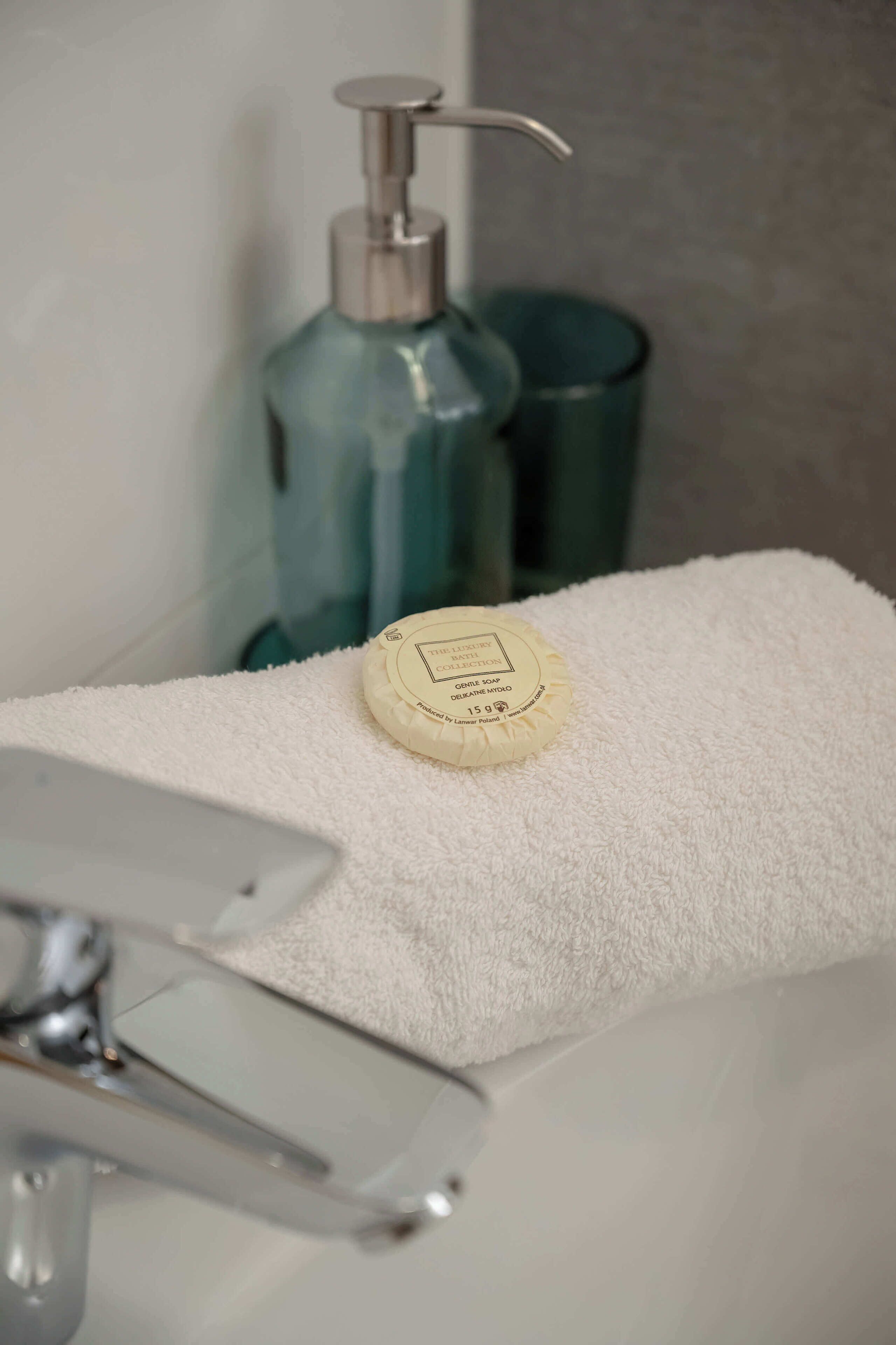 Une salle de bain avec une serviette blanche, un distributeur de savon et un récipient en métal.