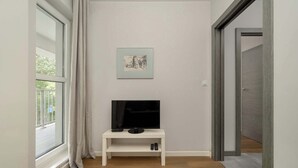 A room with a TV on a white stand, a framed picture on the wall, and a window with curtains. - Stylish Apartment with Balcony | Parking Space (Wrocław)