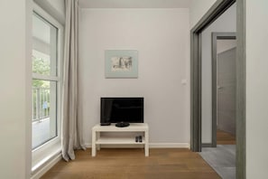A room with a TV on a white stand, a framed picture on the wall, and a window with curtains. - Stylish Apartment with Balcony | Parking Space (Wrocław)