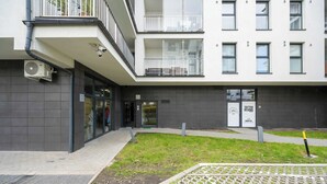 A modern building with a flat roof, multiple balconies, and a small courtyard with grass and a patterned pavement. - Stylish Apartment with Balcony | Parking Space (Wrocław)