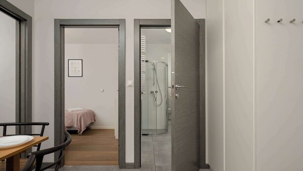 A hotel room with a bed, a small table, a chair, a shower, and a door leading to another room. - Stylish Apartment with Balcony | Parking Space (Wrocław)