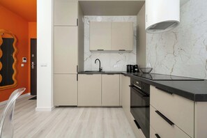 A modern kitchen with light-colored cabinets, a black countertop, and a marble backsplash.