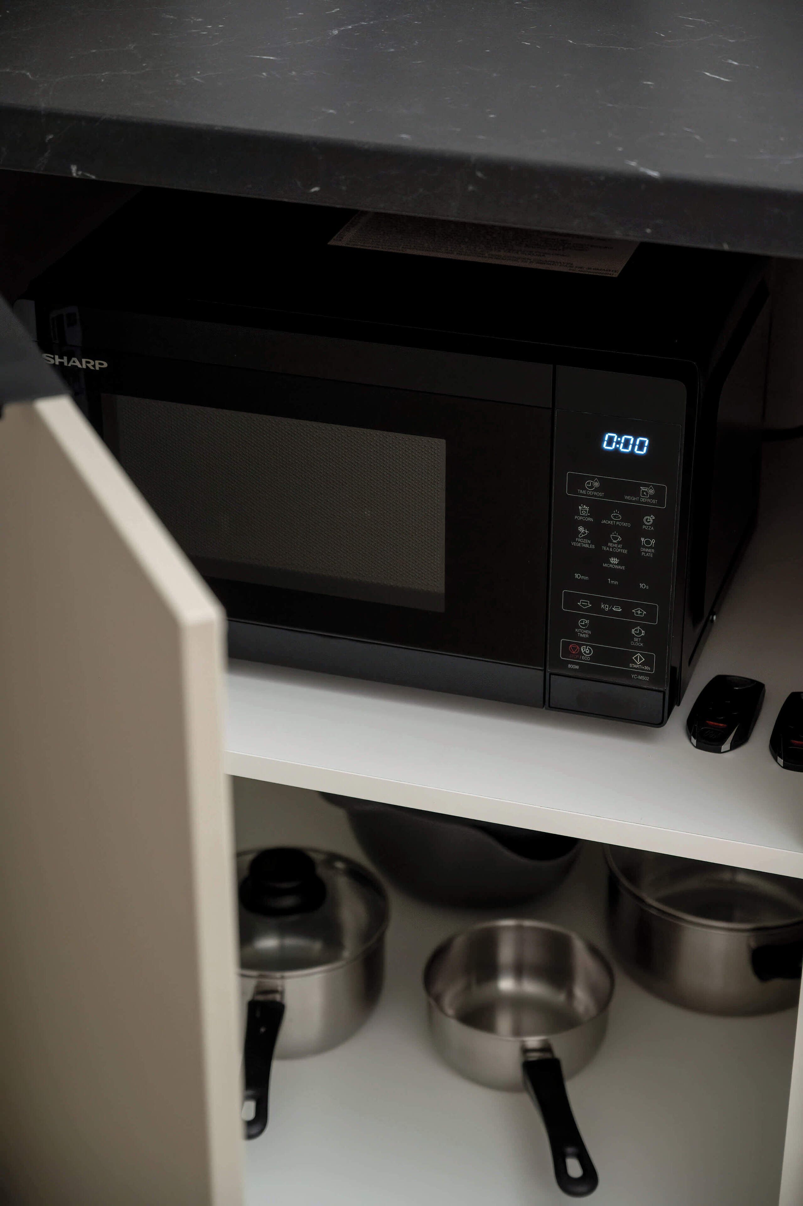 Une cuisine équipée d’un four à micro-ondes, d’une horloge numérique et d’ustensiles de cuisine en acier inoxydable.