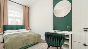 A bedroom with a green bed, white nightstands, a desk with a mirror, and a green chair. - Spacious Apartment in the City Center | Balcony | 2 Bedrooms (Łódź)
