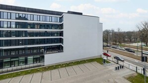 Ein modernes Gebäude mit mehreren Stockwerken, großen Fenstern und einem Parkplatz.