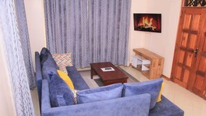 Ein Wohnzimmer mit einer Sofagarnitur, einem Couchtisch und einem an der Wand befestigten Fernseher.