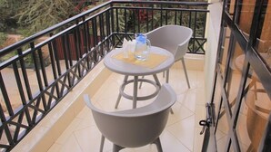 Ein Balkon mit Tisch und zwei Stühlen, einer Wasserkaraffe und einem Glas auf dem Tisch.