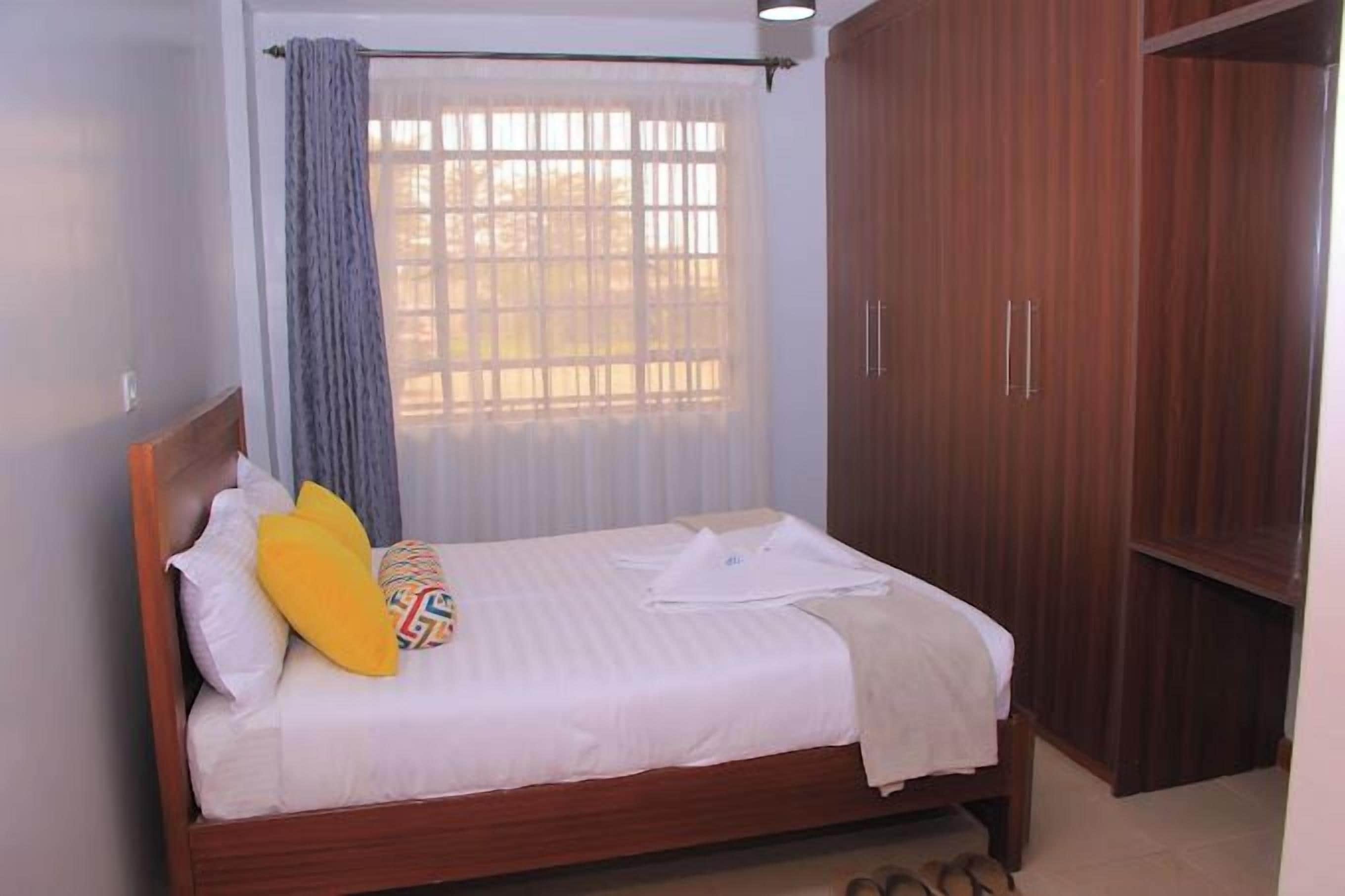 A single bed with white bedding, a wooden headboard, and a window with a curtain.
