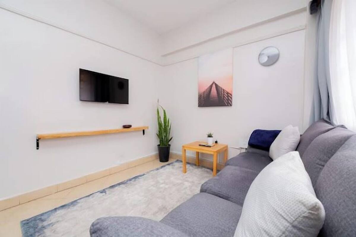 Un saló modern amb un sofà gris, un televisor penjat, una taula de fusta petita i una planta en test.