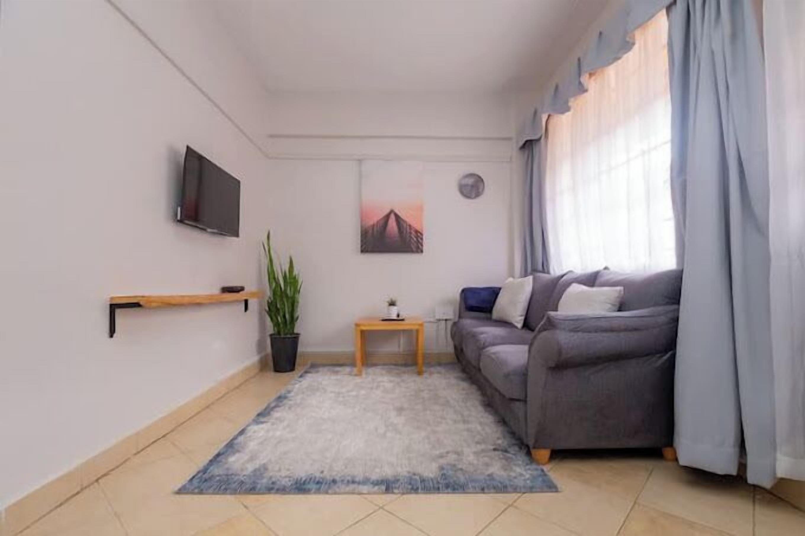 A living room with a grey sofa, a small table, a plant, a mounted TV, and a painting on the wall.