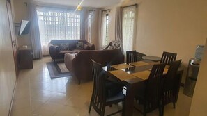 Uma sala de estar com um sofá, uma mesa de jantar com cadeiras e um dispensador de água.
