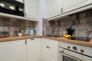 Una cocina con alacenas blancas, microondas, tostadora, pileta y estufa.