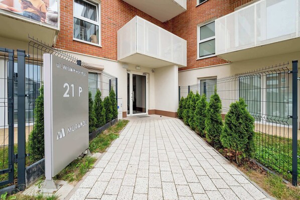 A residential building with a paved entrance, a sign indicating unit 21P, and a gated area with a metal fence.