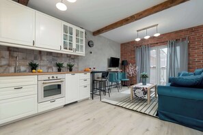 A modern kitchen with white cabinets, a built-in oven, and a dining area with a table and chairs. - Stylish Studio with Balcony | Private Parking and Workspace (Łódź)