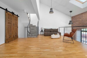 Een ruime loft met houten vloer, een trap, een bank, een salontafel en uitzicht door grote ramen.