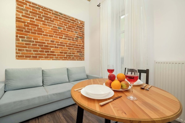 A cozy living area with a light gray sofa, a round wooden coffee table, and an exposed brick accent wall.