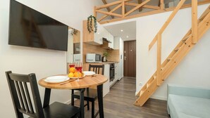 Een moderne keuken met houten balken, een eettafel met stoelen en een aan de muur bevestigde televisie.