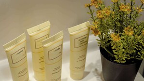 Vier flessen 'The Luxury Bath Collection' shampoo en douchegel, en een potplant met gele bloemen.