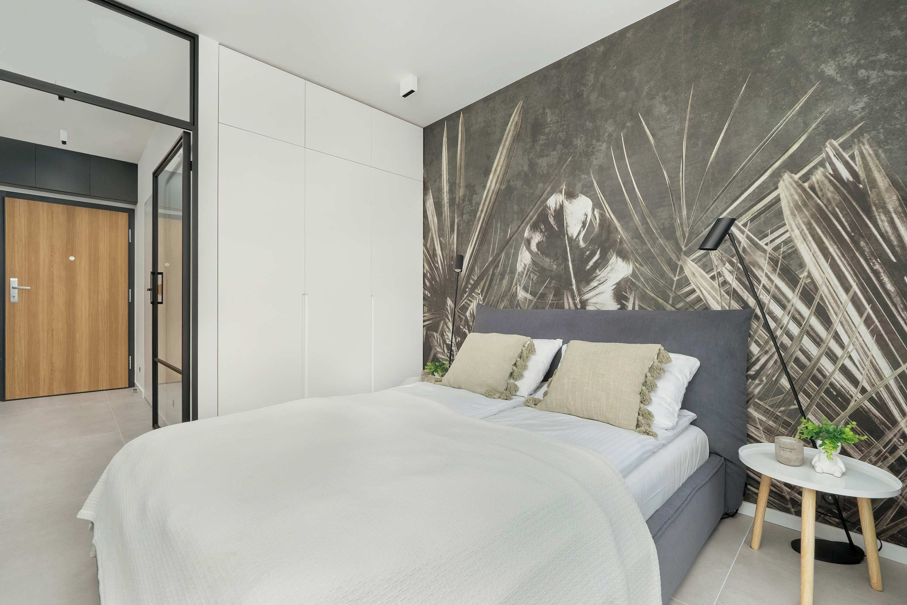 A modern bedroom with a large bed, a round side table, and a wall with a leaf pattern.