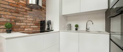 A modern kitchen with white cabinets, a brick wall, a coffee machine, a sink, and a small plant.