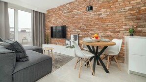 Ein modernes Wohnzimmer mit einem grauen Sofa, einem Esstisch mit weißen Stühlen, einer Ziegelwand und einem Flachbildfernseher.
