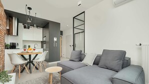 Ein modernes Wohnzimmer mit grauem Sofa, einem Esstisch mit Stühlen und einer Küchenzeile.