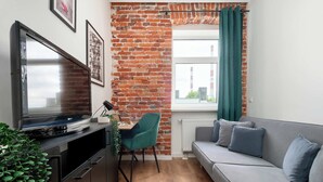 Un espacio habitable pequeño con pared de ladrillo, un sofá, un televisor y un escritorio con silla.