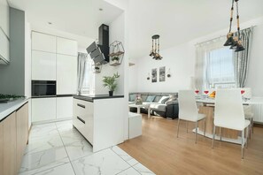 Una cocina moderna con armarios blancos, encimera negra y una mesa de comedor de madera con sillas blancas.