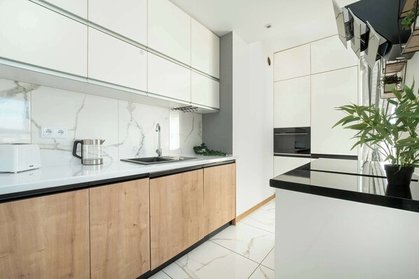 A modern kitchen with white cabinets, a marble backsplash, and a black countertop.