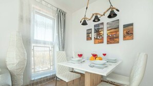 A dining area with a white table set for four, white upholstered chairs, and a window with sheer curtains.