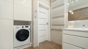 A modern laundry room with a Samsung washing machine, a white door with horizontal lines, and a vanity with a mirror and countertop.