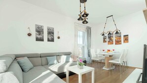 A modern living room with a grey sofa, a white coffee table, and a dining area with a white table and chairs.