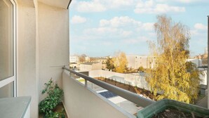 A balcony with a view of buildings and trees, a railing, and a potted plant.
