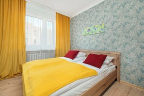 Una camera da letto con un letto, tende gialle, una finestra e una parete decorata con un motivo floreale.