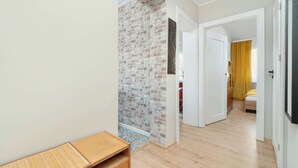 A hallway with a brick wall, wooden flooring, and a bed with a yellow curtain in the background.