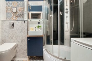 Une salle de bain comprenant des toilettes, un lavabo, une douche avec une porte en verre et un mur décoratif recouvert de carreaux.