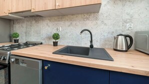 A kitchen with wooden cabinets, a stainless steel sink, a kettle, and a stove.