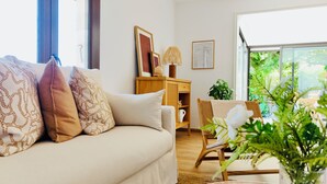 A cozy living room with a sofa, a wooden side table, and a chair. There is a window with a view of greenery outside. - Lili - Pool & View of Lake Carcès (Carcès)