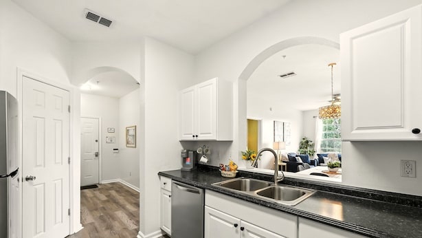 A kitchen with white cabinets, a black countertop, and a stainless steel sink. - Epic Windsor Palms Resort Retreat (Kissimmee)