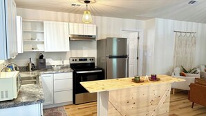 A modern kitchen with white cabinets, a stainless steel refrigerator, a built-in oven, and a wooden island with a coffee maker and jars. - Southern Charm Under the Oaks - Pet Friendly (Ocean Springs)