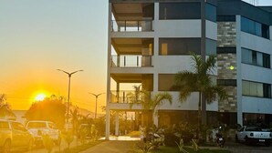 Un edificio a più piani con balconi, auto parcheggiate e un tramonto sullo sfondo.