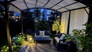 An outdoor patio with a covered seating area, patterned rug, and string lights. - Ravenwood (Niagara-on-the-Lake)
