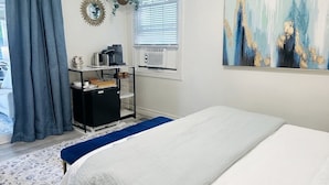 A bedroom with a bed, a desk with a computer, a window with blinds, and a painting on the wall. - Ravenwood (Niagara-on-the-Lake)