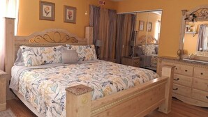 A bedroom with a bed, wooden headboard, a ceiling fan, a dresser, and a mirror. - Three Sisters Cottages (Crystal River)