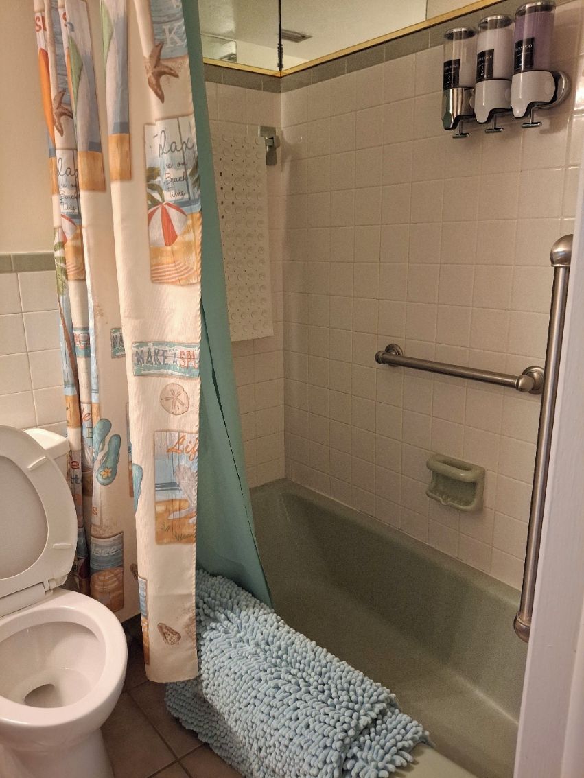 Une salle de bain avec une douche, des toilettes et un porte-serviettes sur lequel sont posées des bouteilles.