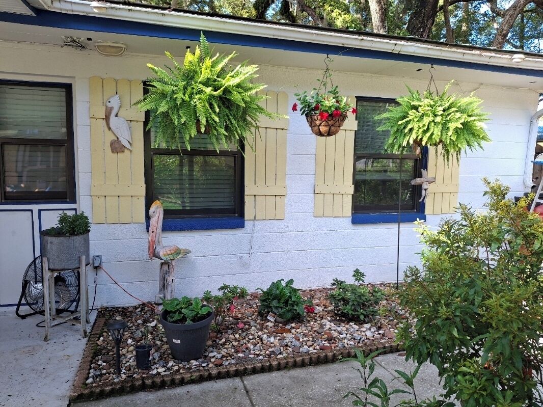 A house with a garden area, a bird sculpture, and hanging planters.