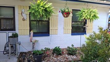 A house with a garden area, a bird sculpture, and hanging planters.