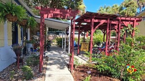 A covered outdoor area with a red pergola, a pathway, and various plants and flowers. - Three Sisters Cottages (Crystal River)