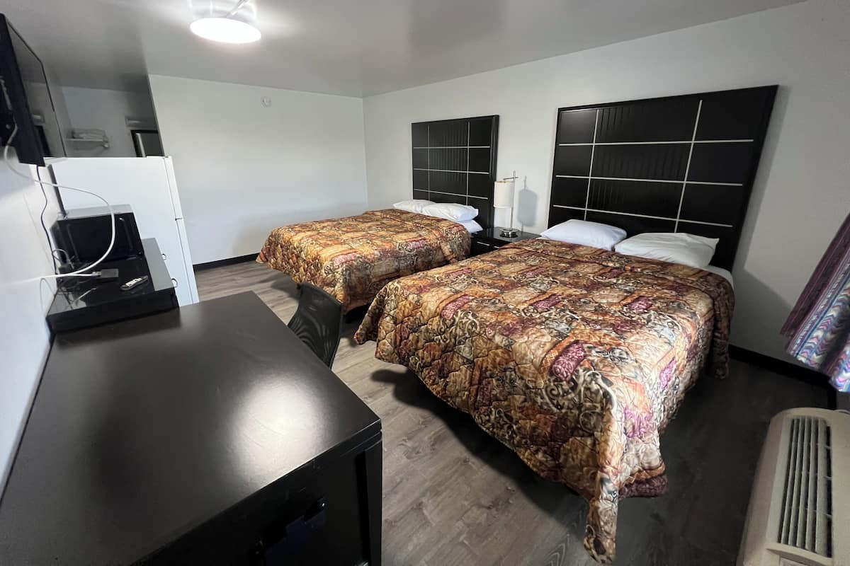 A hotel room with two beds, a desk, and a television.